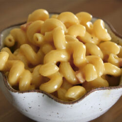 Homemade macaroni and cheese a white bowl with cavatappi pasta and melted cheddar sauce.