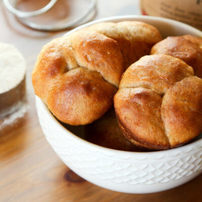 A bowl filled with golden brown, freshly baked No Knead Cloverleaf Rolls.