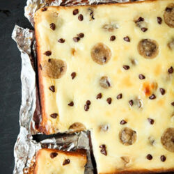 Overhead view of a foil-lined pan of chocolate chip cheesecake brownies with a corner piece cut out.