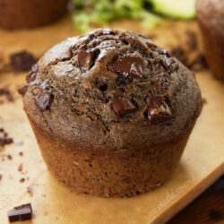 Close-up of chocolate chunk zucchini muffin on a wooden surface.