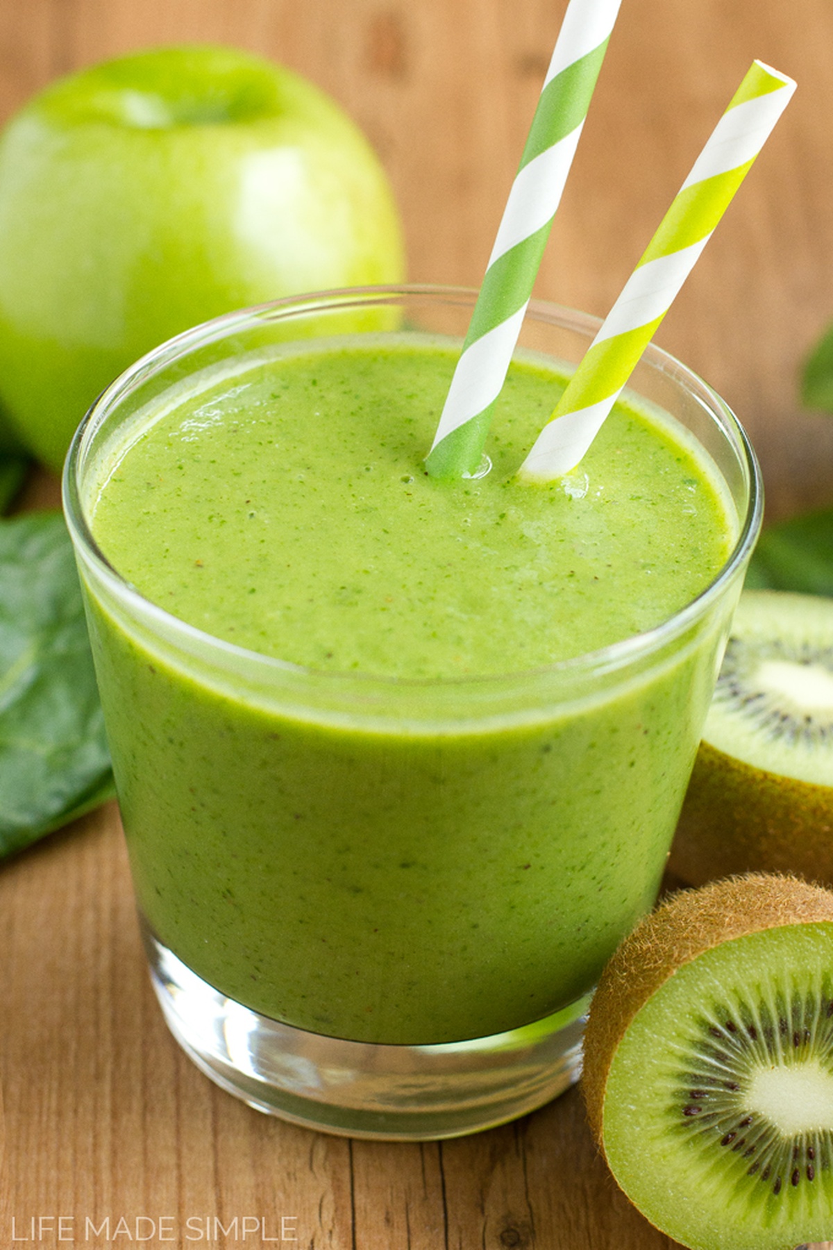 Top-down view of a green monster smoothie in a glass with striped straws.