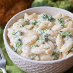 A bowl of white cheddar pasta served with broccoli florets and cheese sauce.