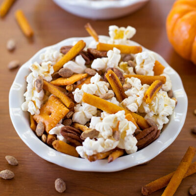 A white bowl filled with an autumn snack mix on a wooden surface.