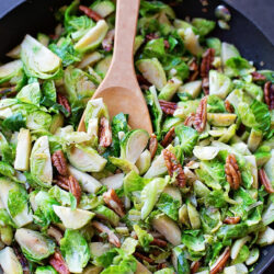 Bacon maple brussels sprouts in a skillet with a wooden spoon.