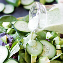 Green goddess yogurt dressing being poured from a glass jar onto a fresh green salad.