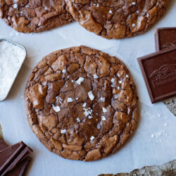 Gluten free dark chocolate cookies topped with sea salt flakes on parchment paper.