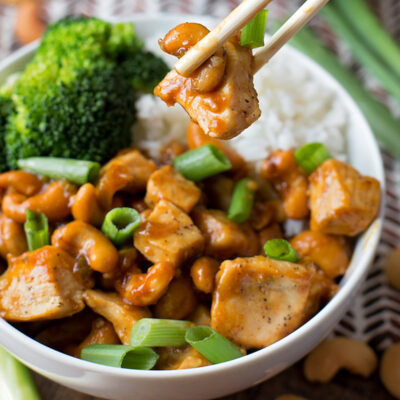 A simple cashew chicken being picked up with chopsticks from the bowl.