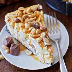 A slice of no-bake Snickers cheesecake on a white plate.