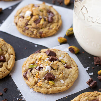 Dark chocolate and pistachio cookies on parchment paper next to a jar of milk.