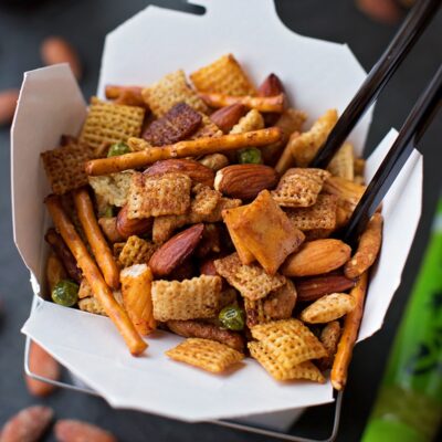 A close-up view of an Asian snack mix in a white takeout box.