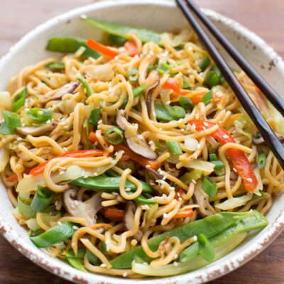 A close-up of a bowl of ramen stir fry garnished with green onions and sesame seeds.