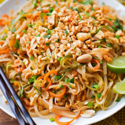 A plate of veggie Pad Thai topped with chopped peanuts and lime wedges.