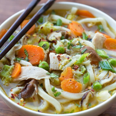 Asian style chicken noodle soup served in a white bowl.