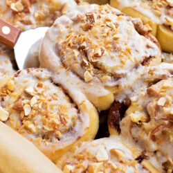 Freshly baked tropical cinnamon rolls topped with cream cheese glaze in a baking pan.