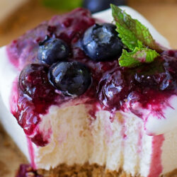 Cheesecake bars no-bake with blueberry compote and mint, partially eaten on a cutting board.