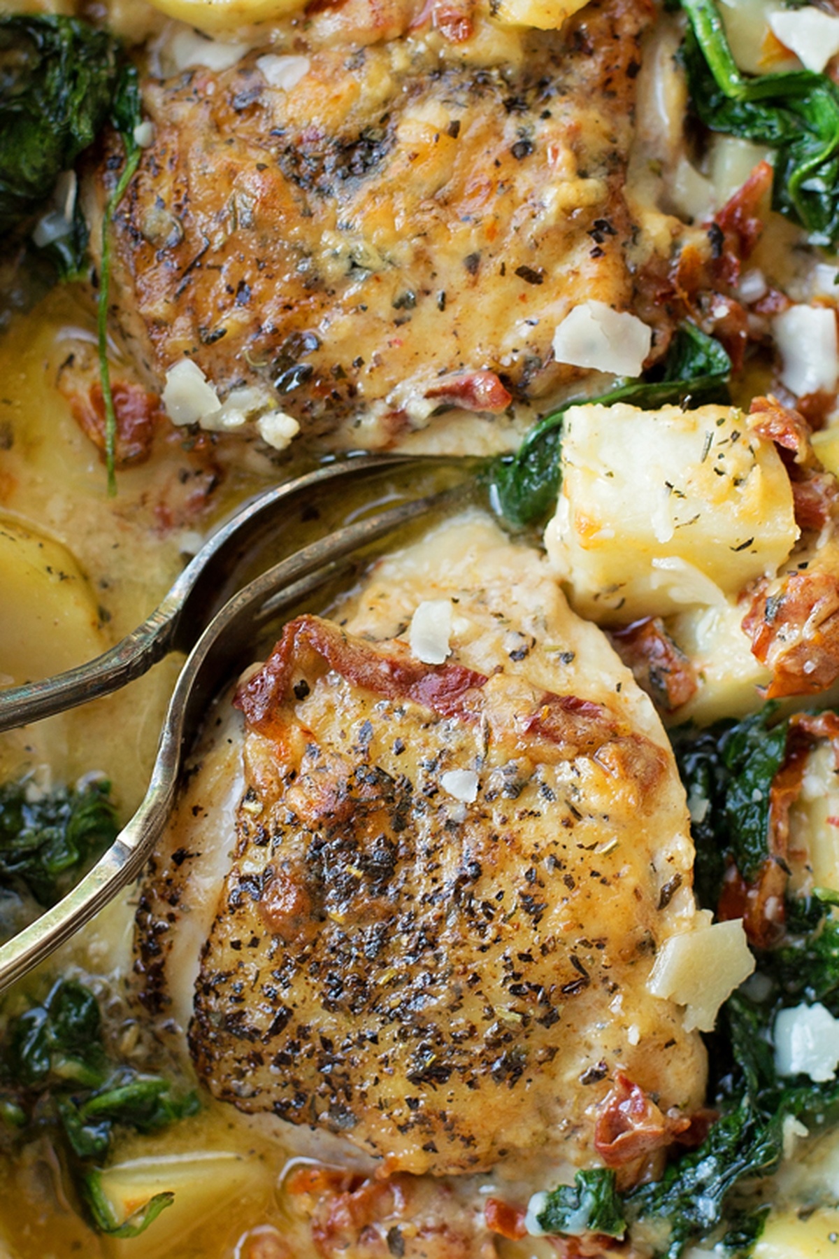 Close-up of seasoned chicken thighs with tender potatoes and spinach, served in a rich Tuscan cream sauce.