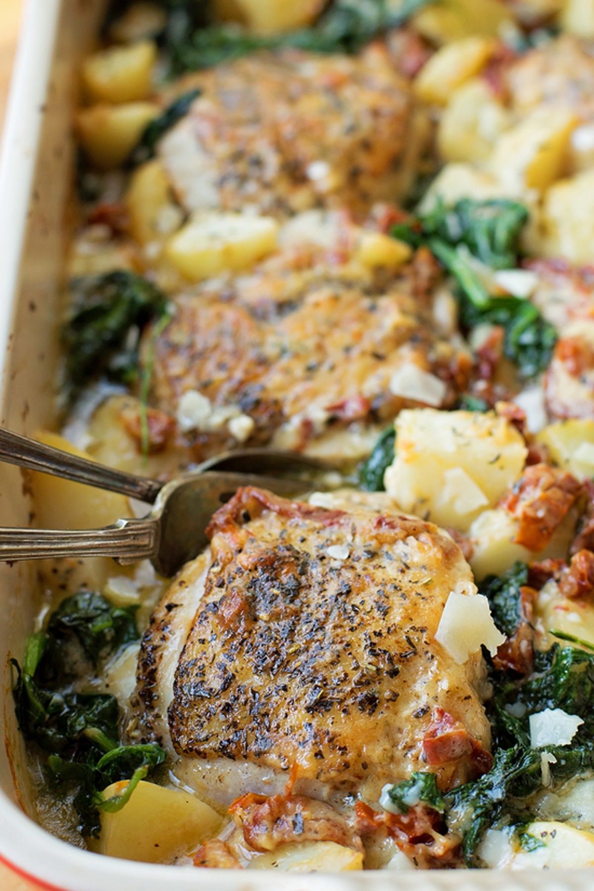 A baking dish filled with creamy Tuscan chicken and potatoes, garnished with spinach and sun-dried tomatoes.