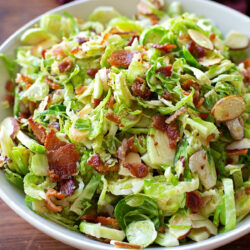 Brussels sprouts salad with bacon and almonds in a white bowl.