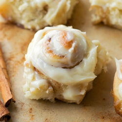 Homemade cinnamon rolls with simple cream cheese icing for cinnamon rolls and cinnamon sticks nearby.