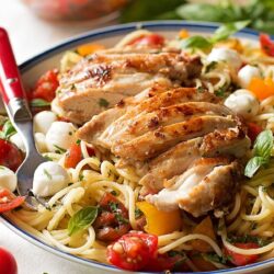 Chicken bruschetta pasta served with sliced chicken over spaghetti, fresh cherry tomatoes, basil, and mozzarella.