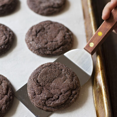 A freshly baked soft chocolate sugar cookie being lifted from a baking sheet with a spatula.