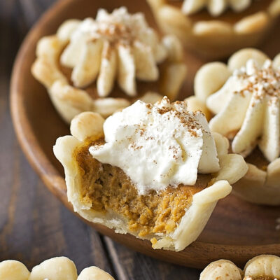 A batch of miniature pumpkin pies, one with a visible bite showing creamy filling.