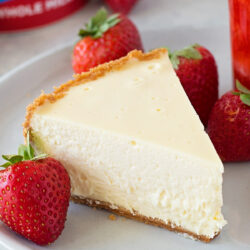 A slice of cheesecake Instant Pot served with fresh strawberries on a white plate.