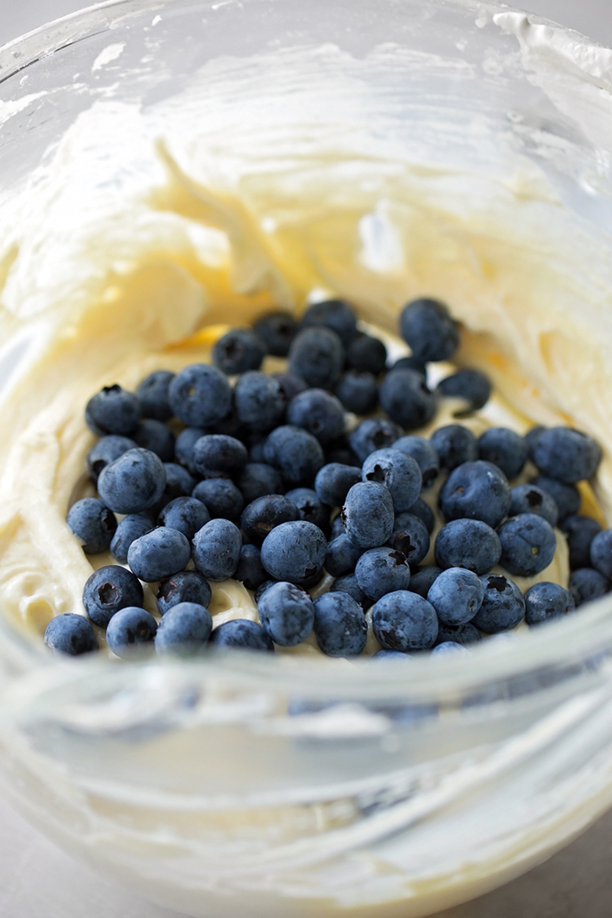 Fresh blueberries folded into the creamy cake batter in a glass mixing bowl.