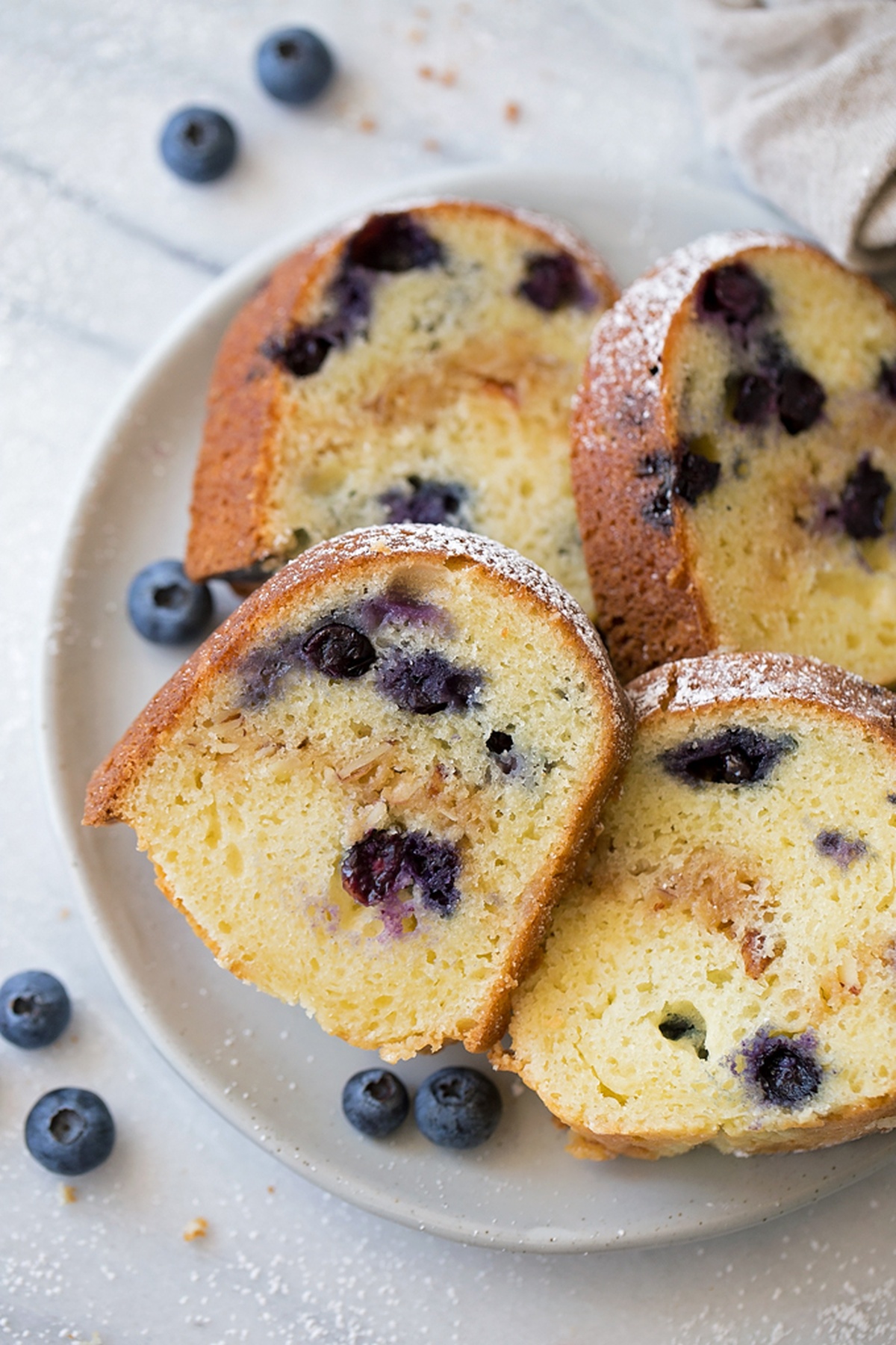 Several slices of Blueberry Almond Bundt Cake arranged on a plate with fresh blueberries scattered around.
