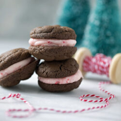 Three peppermint sandwich cookies stacked in front of holiday decorations.