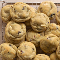 A wire rack loaded with freshly baked white chocolate cranberry pistachio cookies.