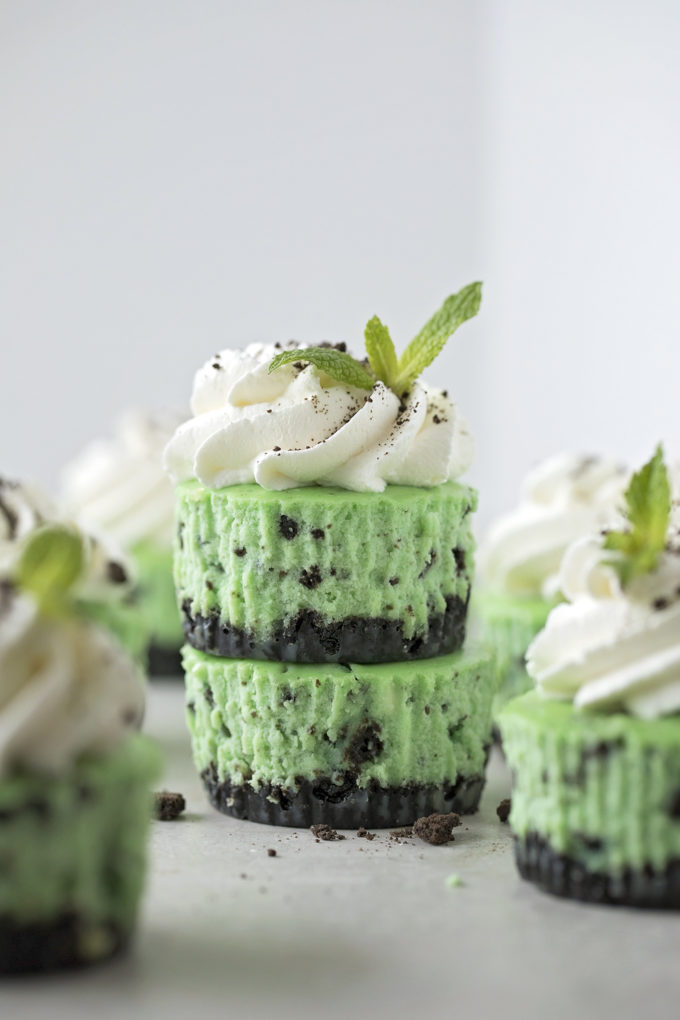 A stack of mini mint oreo cheesecakes garnished with homemade whipped cream, cookie crumbs, and a sprig of mint.