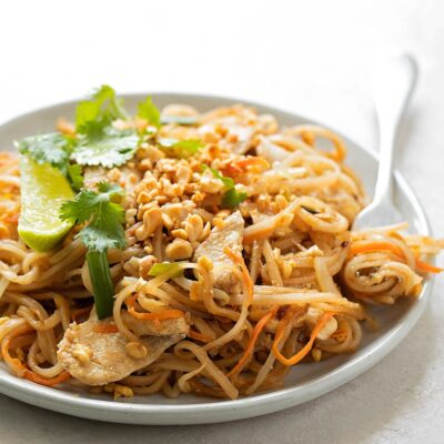 A plate of Pad Thai, garnished with lime, cilantro, and crushed peanuts.
