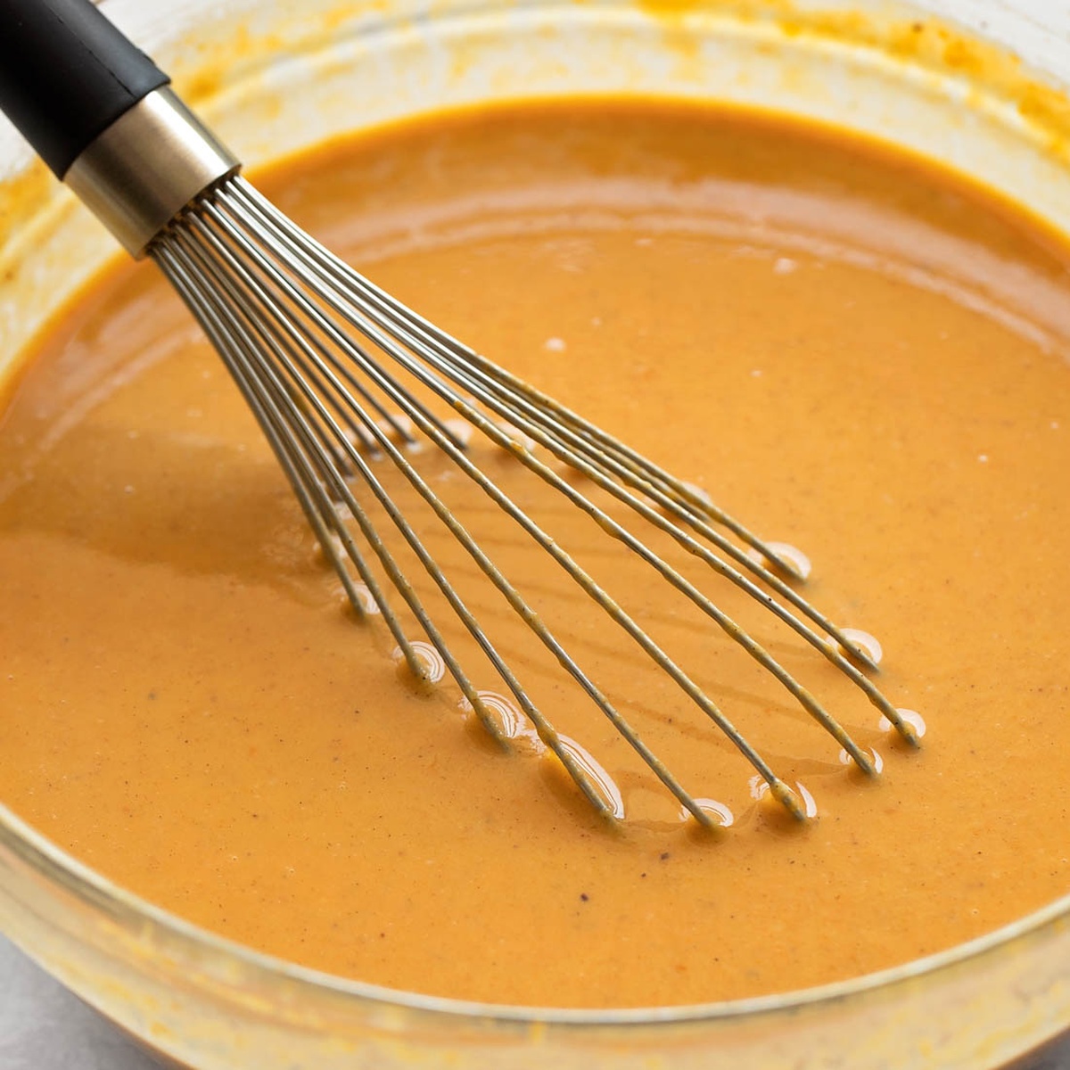 A bowl of spiced pumpkin custard with a whisk.