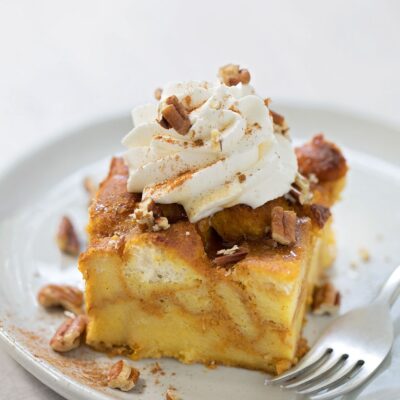 A slice of pumpkin bread pudding topped with whipped cream and pecans.