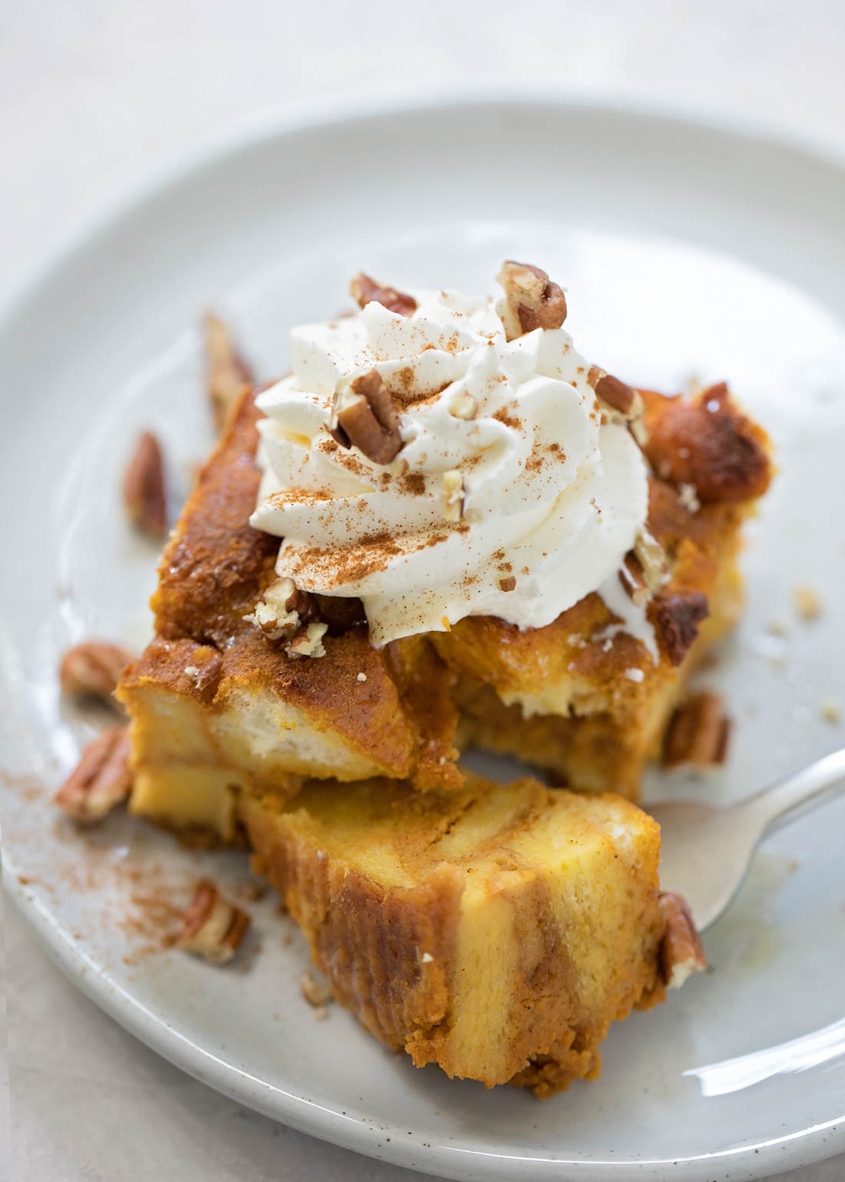 A serving of pumpkin bread pudding topped with whipped cream and pecans on a plate.