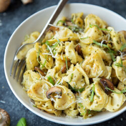 A bowl of tortellini with mushrooms and pesto sauce.