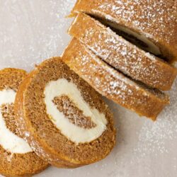 Sliced pumpkin roll revealing the cream cheese swirl, sprinkled with powdered sugar.