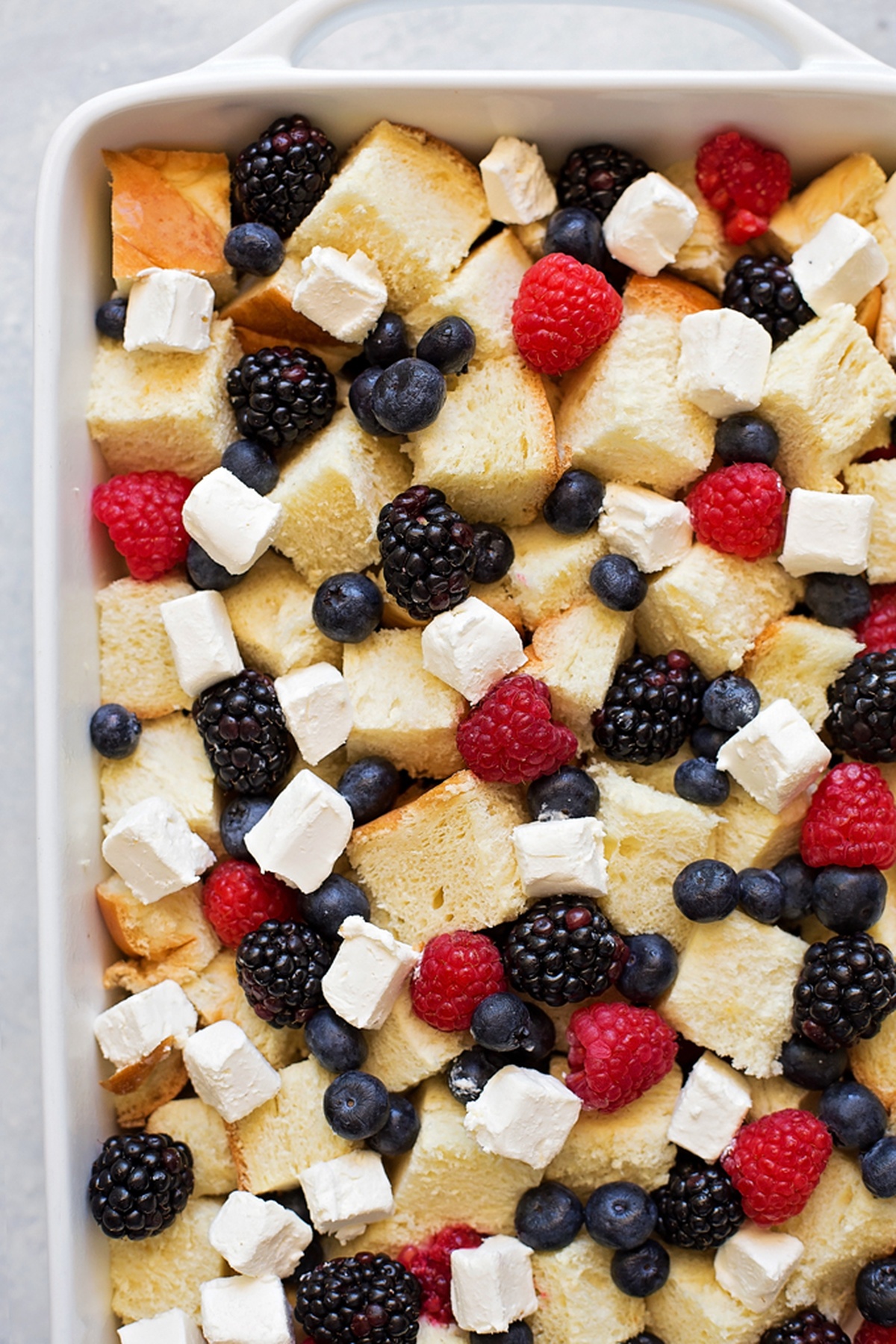 Bread cubes layered with cream cheese and fresh berries in a baking dish.