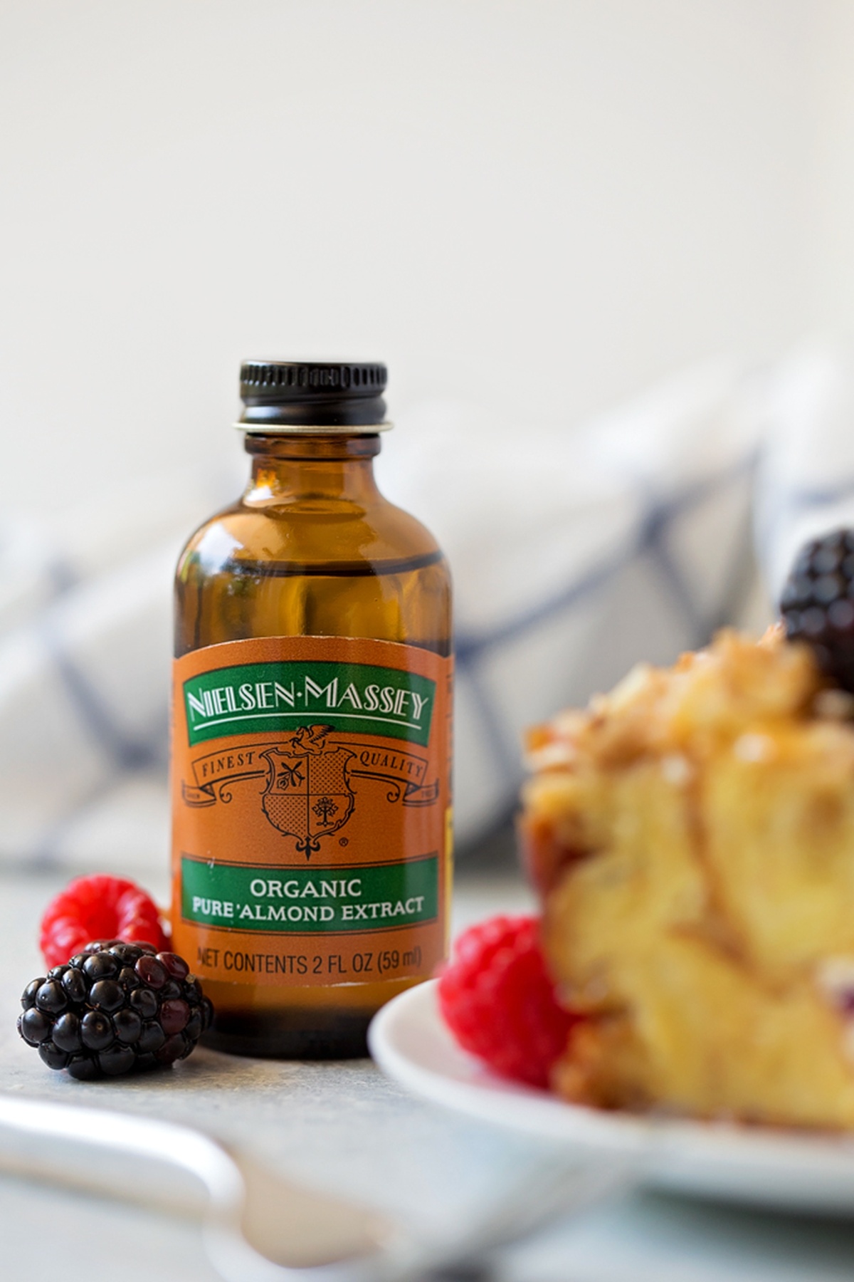 A bottle of almond extract next to the baked casserole and fresh berries.