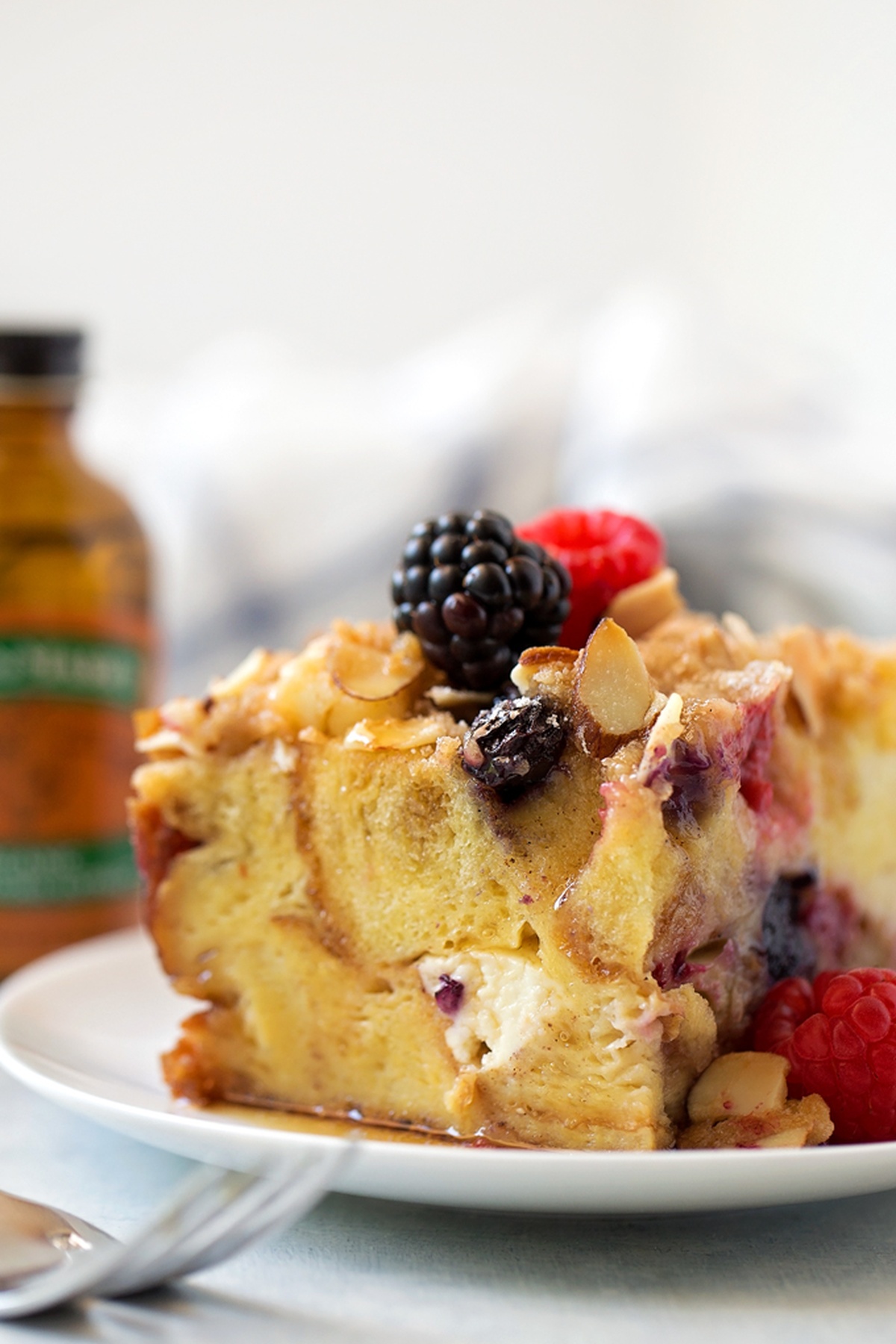 A slice of Berry French Toast Casserole on a white plate with maple syrup drizzled on top.