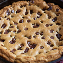 A freshly baked brown butter skillet cookie with golden edges and melted chocolate chips in a cast iron skillet.