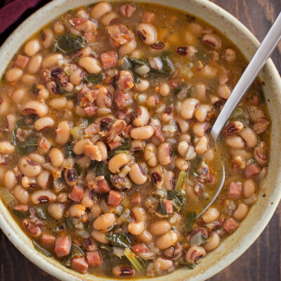 A bowl of black-eyed pea soup with chunks of ham and greens.