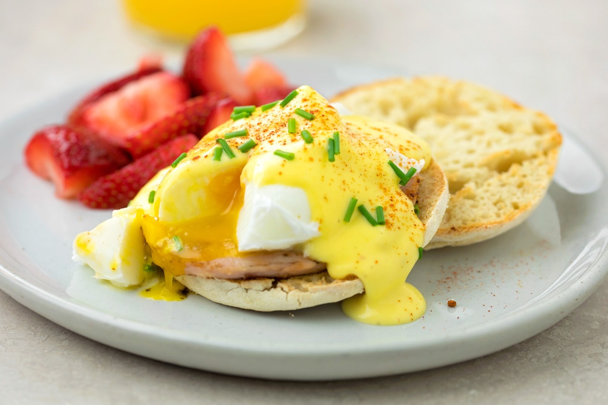 Eggs Benedict-the breakfast classic made at home! You will love our creamy and tangy hollandaise sauce over top of your poached eggs, crisp Canadian bacon and toasted English muffin! A close-up of Eggs Benedict with a cut poached egg.