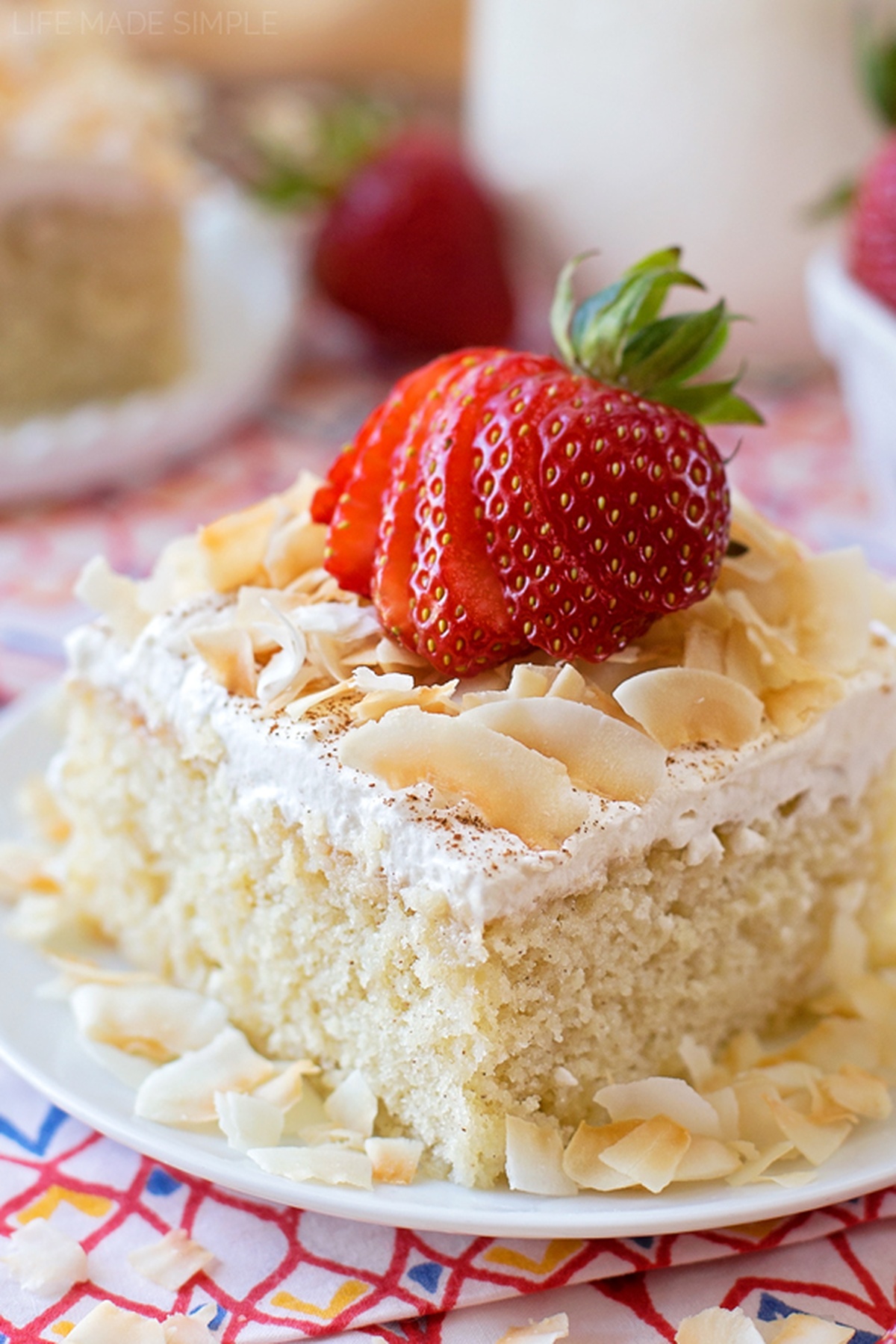 You're going to fall in love this tres leches cake - I did! It's tender, moist and sweet, the perfect treat for your Cinco de Mayo fiesta!! A slice of Tres Leches Cake topped with fresh strawberries and toasted coconut on a white plate.