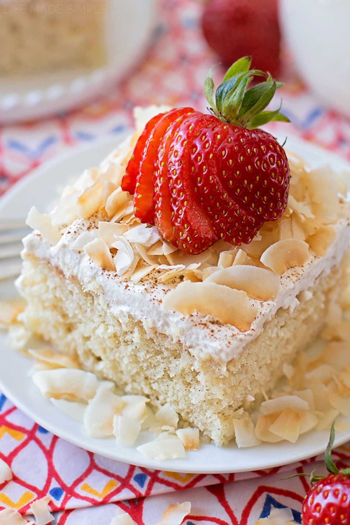You're going to fall in love this tres leches cake - I did! It's tender, moist and sweet, the perfect treat for your Cinco de Mayo fiesta!! A slice of Tres Leches topped with whipped cream, toasted coconut, and a sliced fresh strawberry, served on a plate.