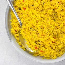 A bowl with yellow rice and a spoon.