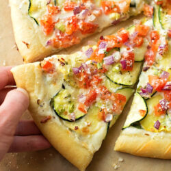 Hand holding a slice of veggie pizza.