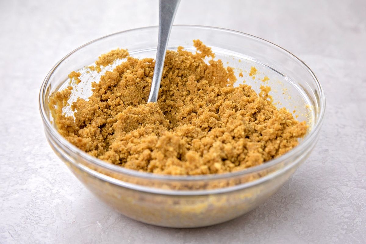 A glass bowl filled with graham cracker crumbs and melted butter being mixed.