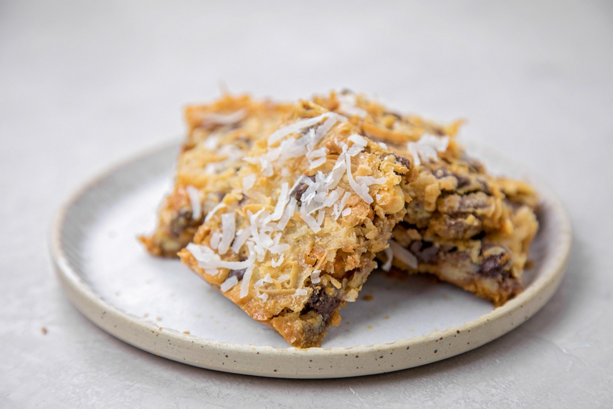 A close-up of two 7 Layer Bars on a plate, topped with shredded coconut. 